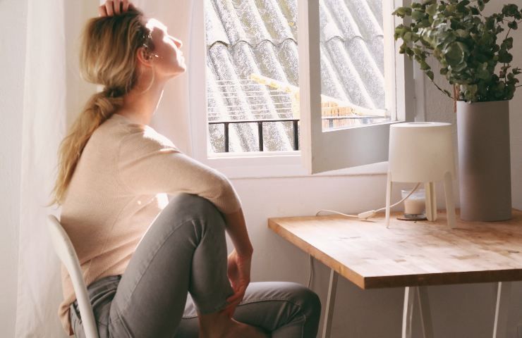 Ragazza guarda fuori dalla finestra con il viso rivolto verso il sole