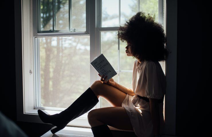 Ragazza afroamericana legge un libro seduta sul bordo della finestra