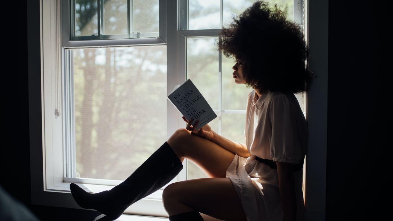 Ragazza afroamericana legge un libro sulla finestra