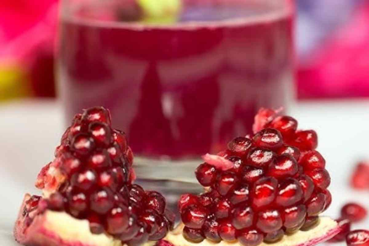 Un melograno aperto a metà e dietro un bicchiere di succo
