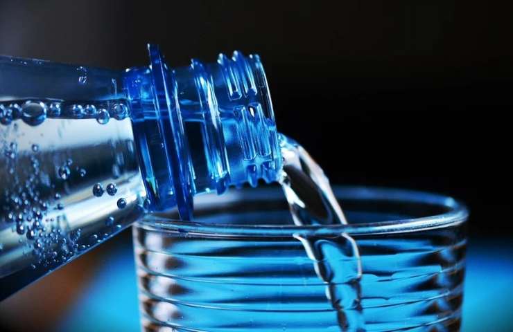 Acqua versata in bicchiere da una bottiglia in plastica