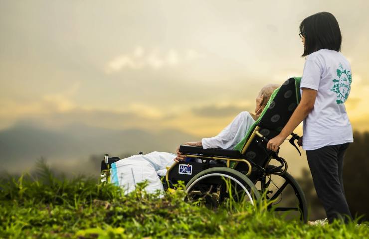 Donna con anziano disabile su sedia a rotelle