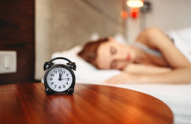 Una donna dorme con una sveglia poco lontano