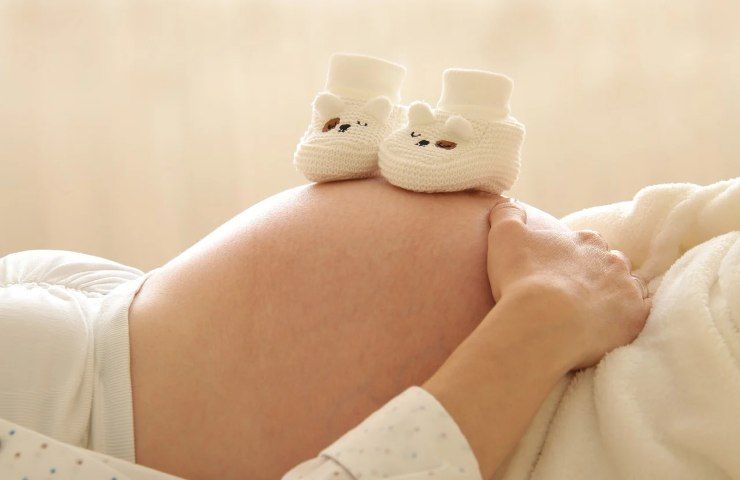 Una donna incinta con delle babbucce per neonato