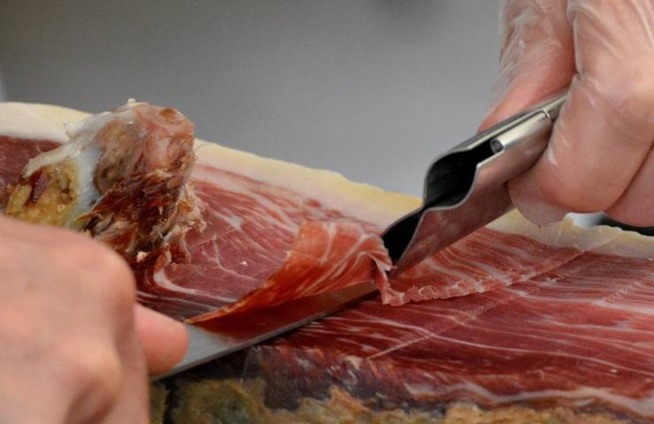 Un uomo affetta del prosciutto crudo