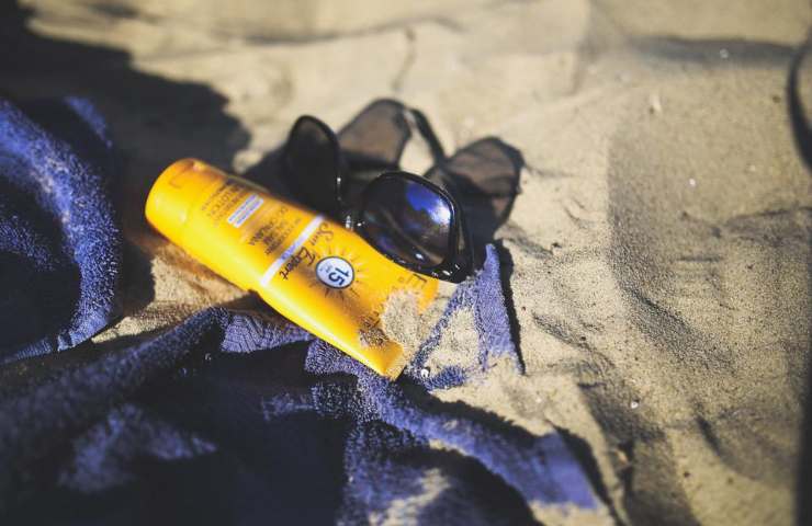 Una crema solare e degli occhiali da sole su un telo in spiaggia