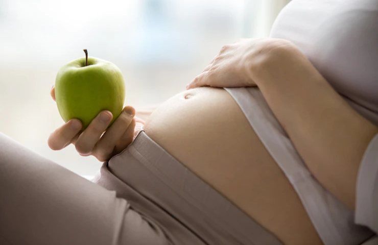 Una donna incinta tiene una mela