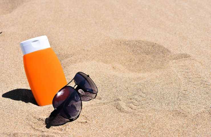 Un flacone di crema solare e degli occhiali da sole in spiaggia