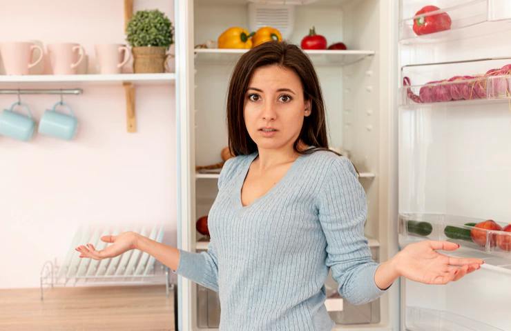 Una donna in posa interrogativa con il frigo aperto