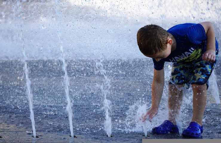 Un bambino gioca trovando sollievo in mezzo ad una fontana
