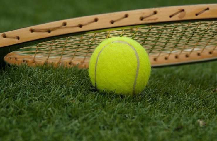 Una racchetta da tennis ed una pallina sull'erba
