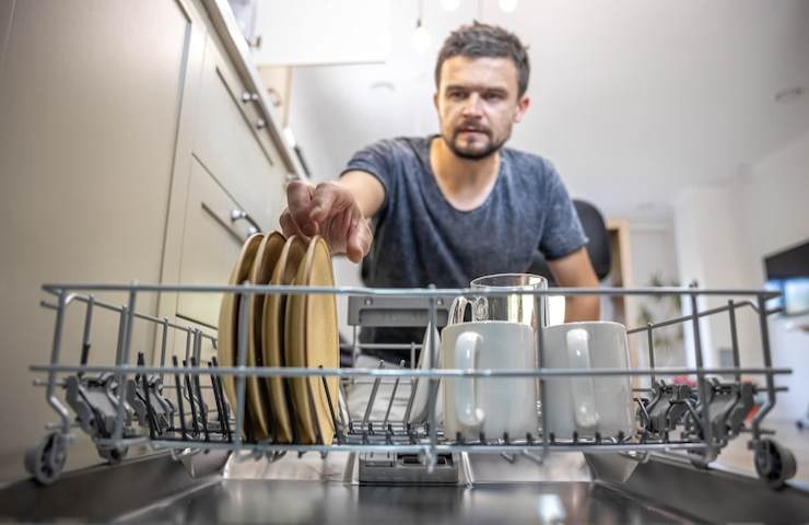 Un uomo estrae dei piatti da una lavastoviglie