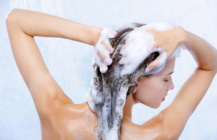 Una donna mentre si lava i capelli sotto alla doccia