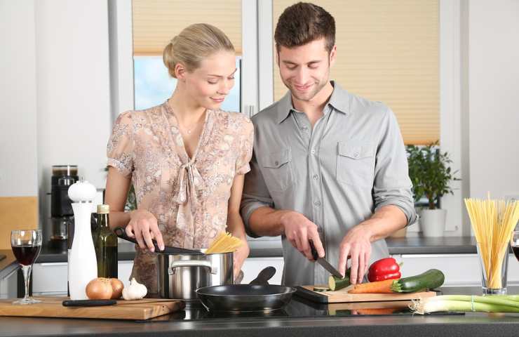 Una coppia impegnata a tagliare degli ortaggi in cucina