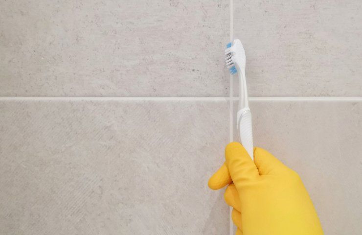 Una persona pulisce le fughe delle piastrelle con uno spazzolino