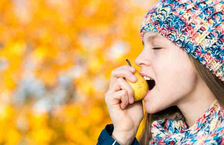 Una ragazza impegnata a mangiare una pera 