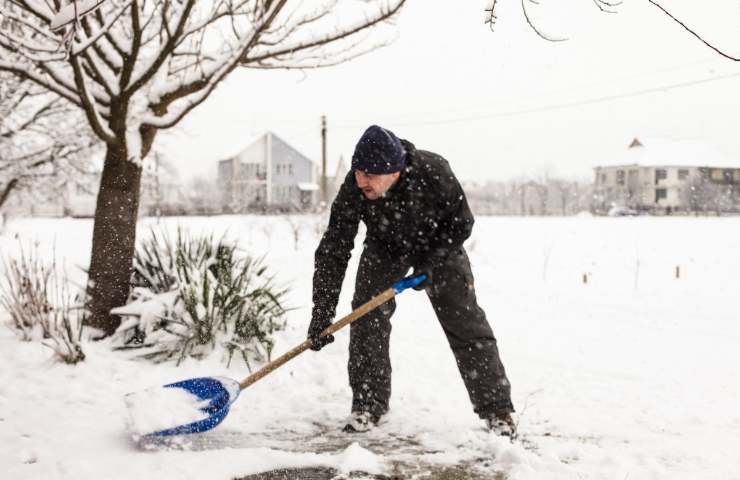 Un uomo impegnato a spalare la neve in giardino