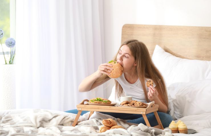 Una ragazza che divora del cosiddetto cibo spazzatura