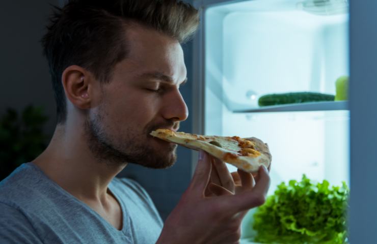 Un uomo che mangia una fetta di pizza di notte