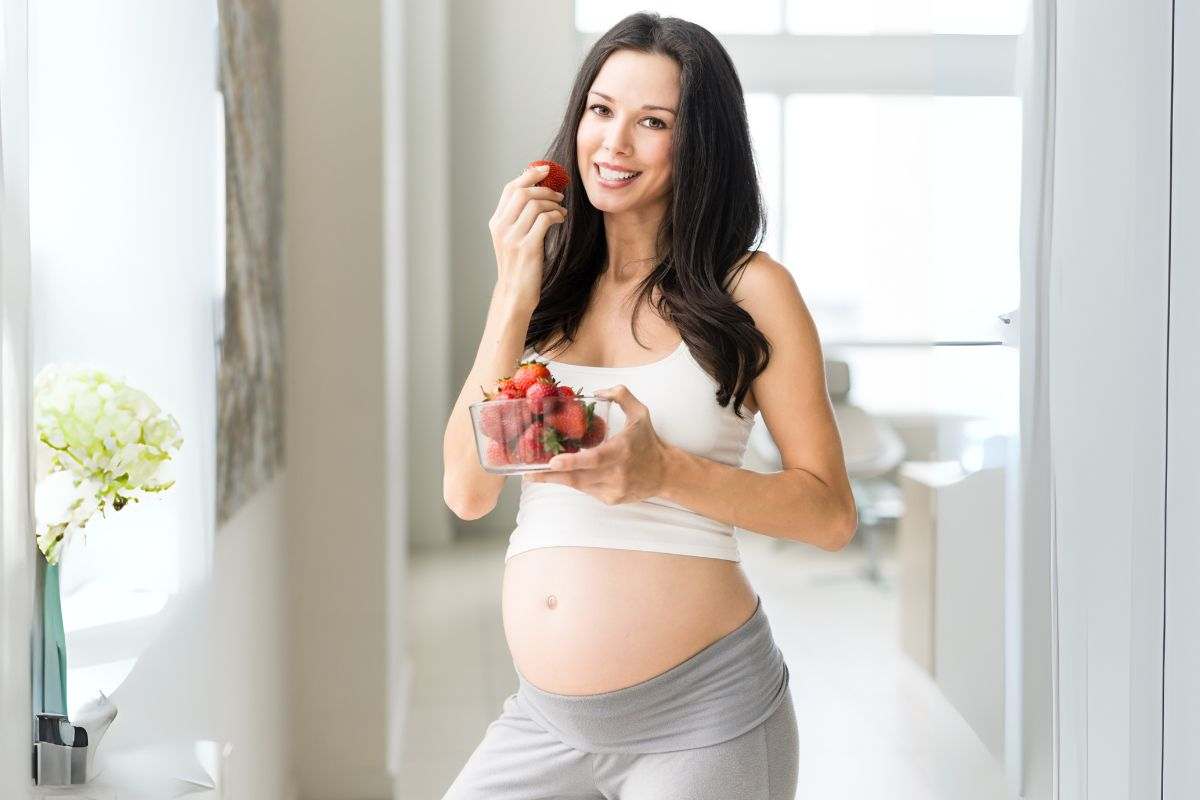 donna in gravidanza che mangia una fragola, in mano ha una vaschetta di fragole