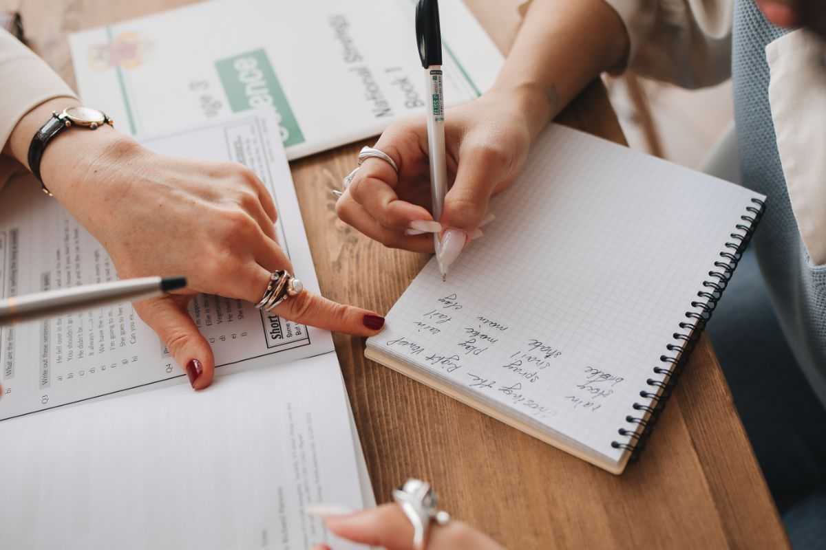 donna che scrive su un quaderno e persona che indica le lettere
