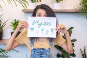 ragazza tra piante verdi in mano cartello con scritto vegan