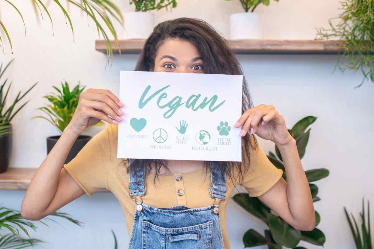 ragazza tra piante verdi in mano cartello con scritto vegan