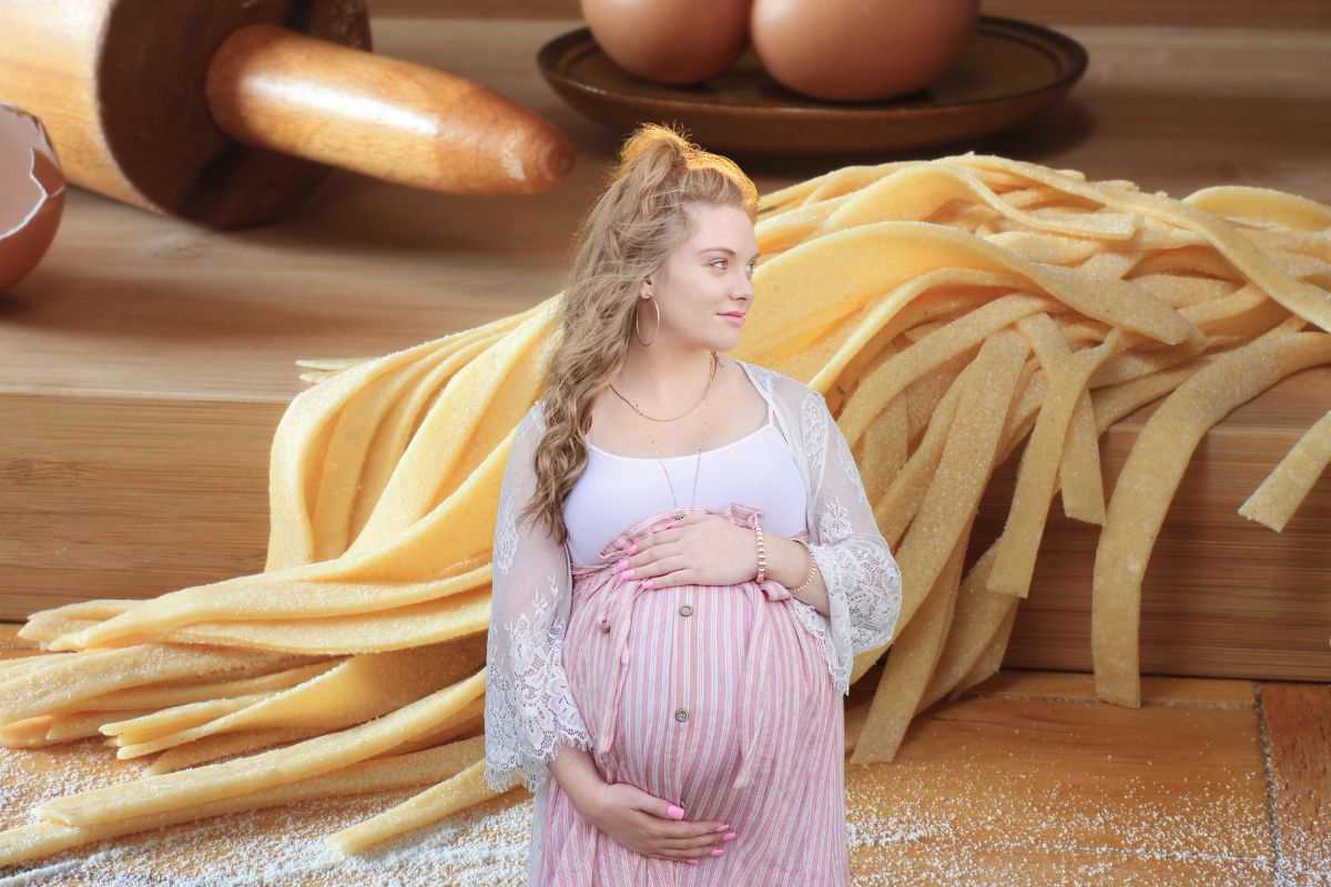 sullo sfondo pasta all'uovo, mattarello, uova e farina, primo piano donna incinta