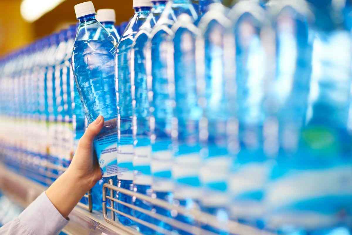 donna che prende una bottiglia di acqua dallo scaffale di un supermercato