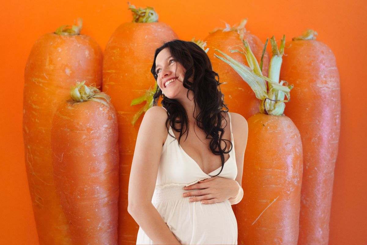 sullo sfondo arancione carote e in primo piano donna incinta sorridente