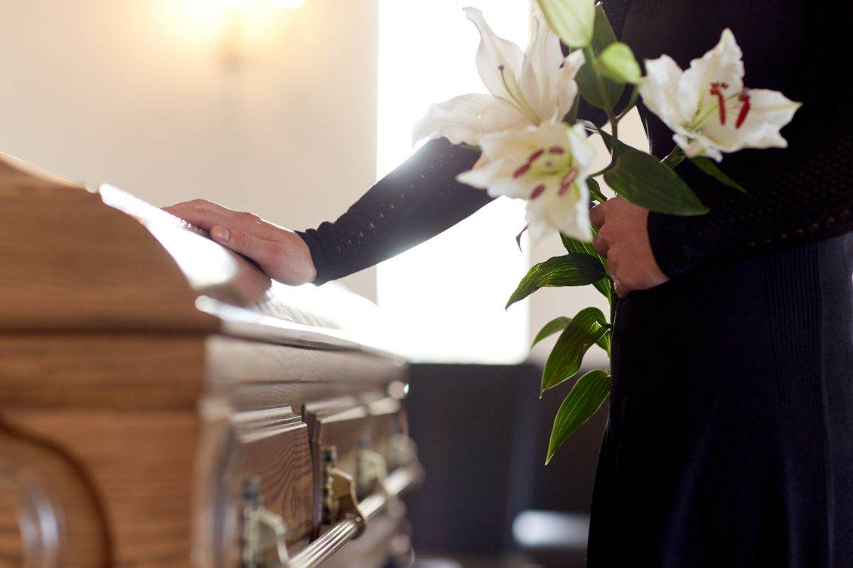 persona che tocca una bara con fiori bianchi in mano