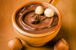 Una ciotola con della crema alla nocciola e delle nocciole intere