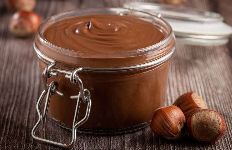 Un vasetto con crema alla nocciola e delle nocciole intere