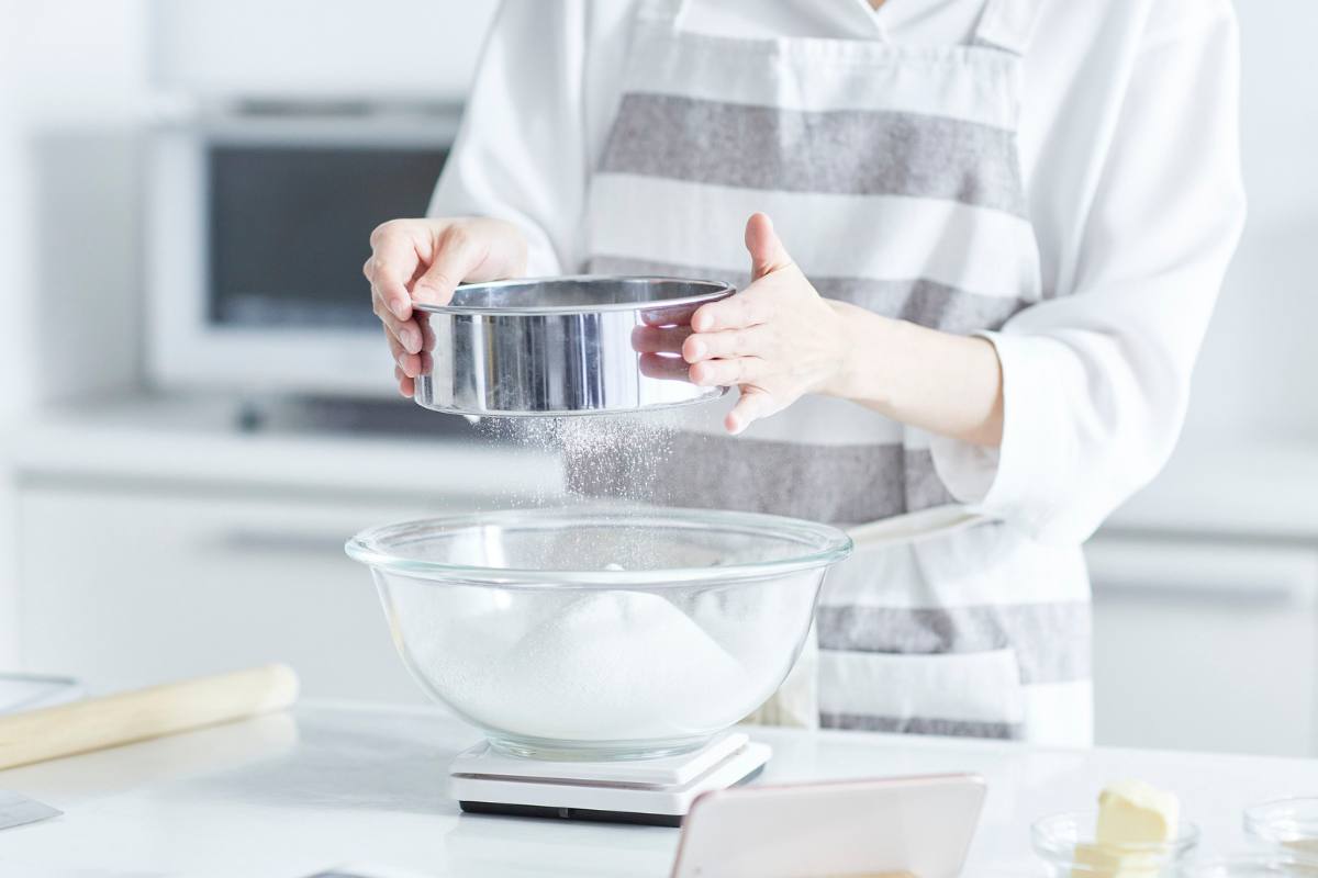 donna prepara torta setacciando farina