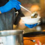 una mano versa la zuppa in una scodella con un mestolo