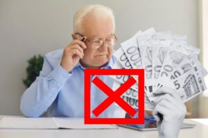 uomo anziano al telefono mentre controlla tablet, con mano in bianco e nero che tiene banconote euro e x rossa sopra