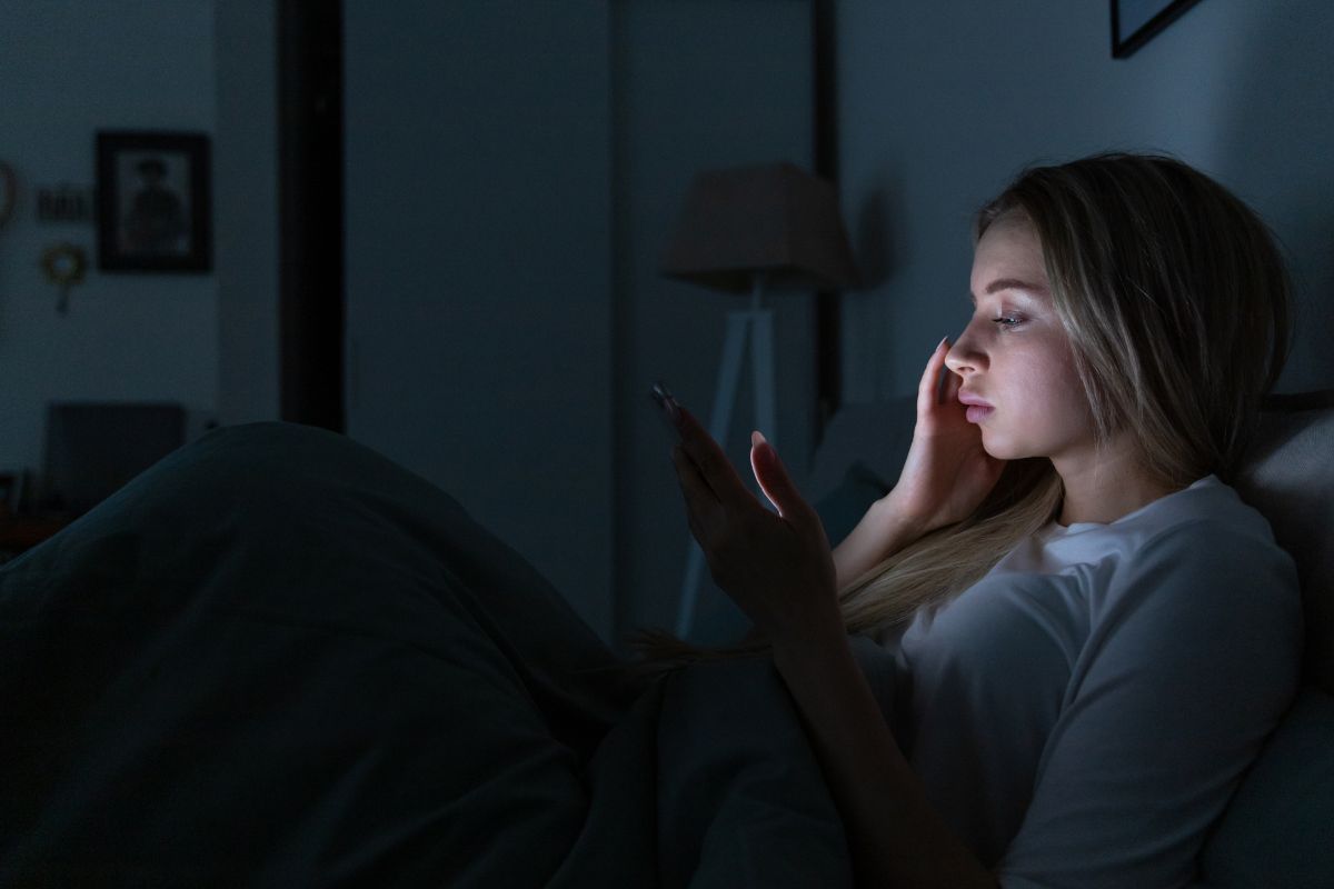 ragazza a letto con lo smartphone in mano