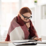 donna davanti al pc con sciarpa che si soffia sulle mani per riscaldarle