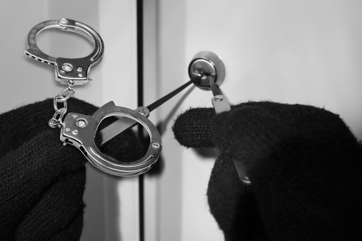 mani di ladro con guanti che scassinano una serratura e delle manette