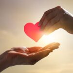 due mani che si passano un cuore di carta rosso