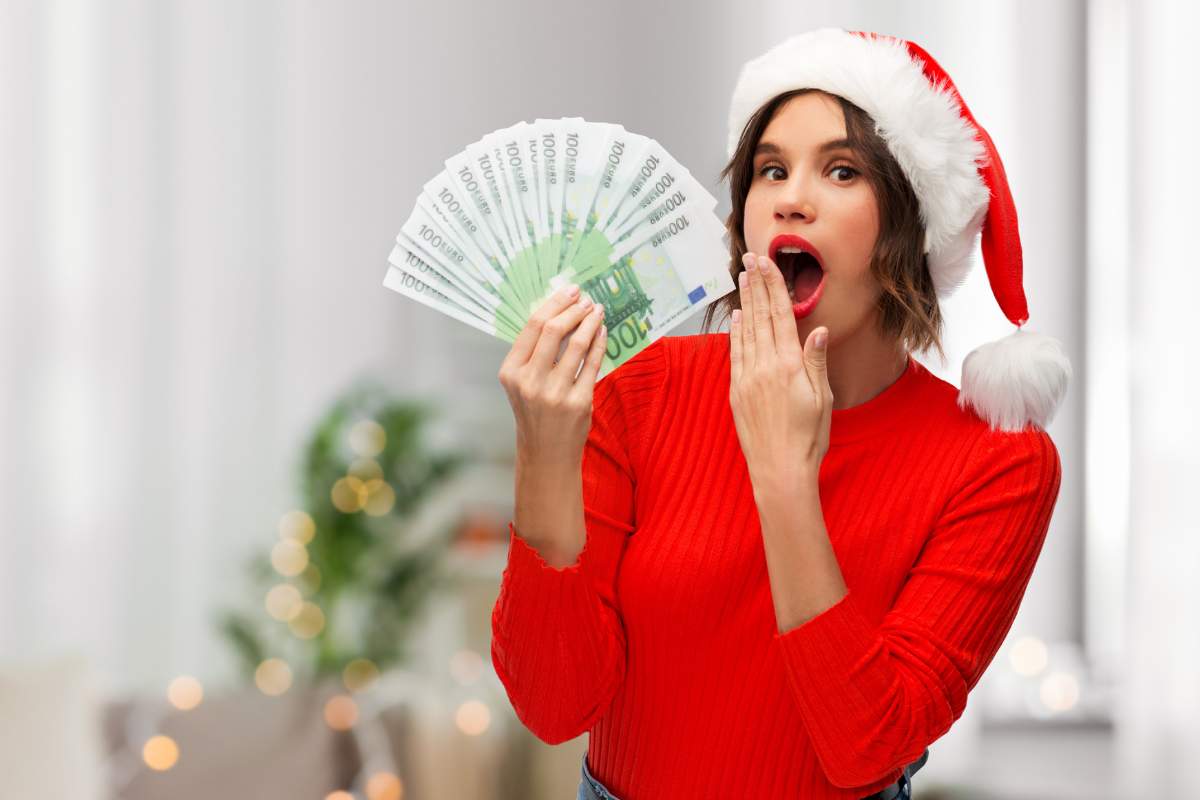 ragazza vestita di rosso e con cappello di babbo natale con soldi in mano