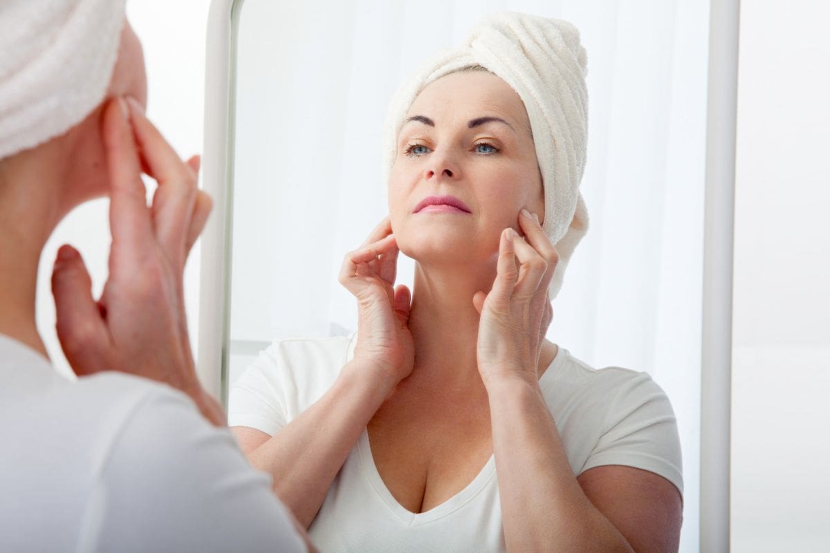 donna di 50 anni che si guarda allo specchio e tira la pelle del viso
